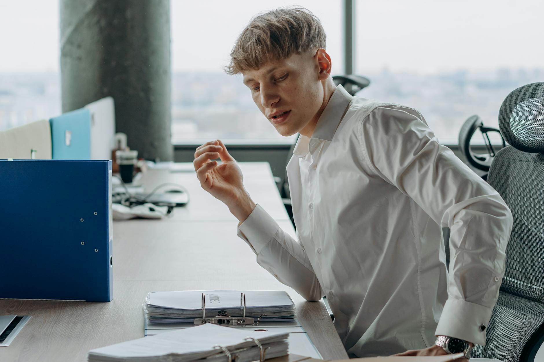 Mężczyzna przy biurku w biurze czyta dokumenty w białej koszuli