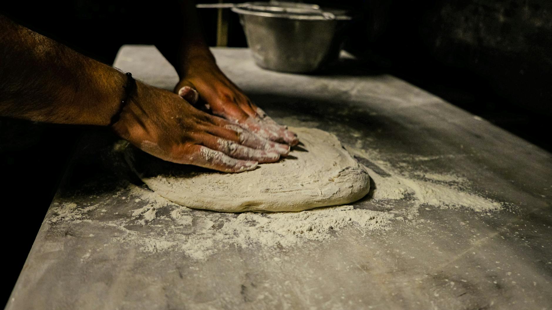 Mężczyzna zagniata ciasto na pizzę na oprószonym mąką stole