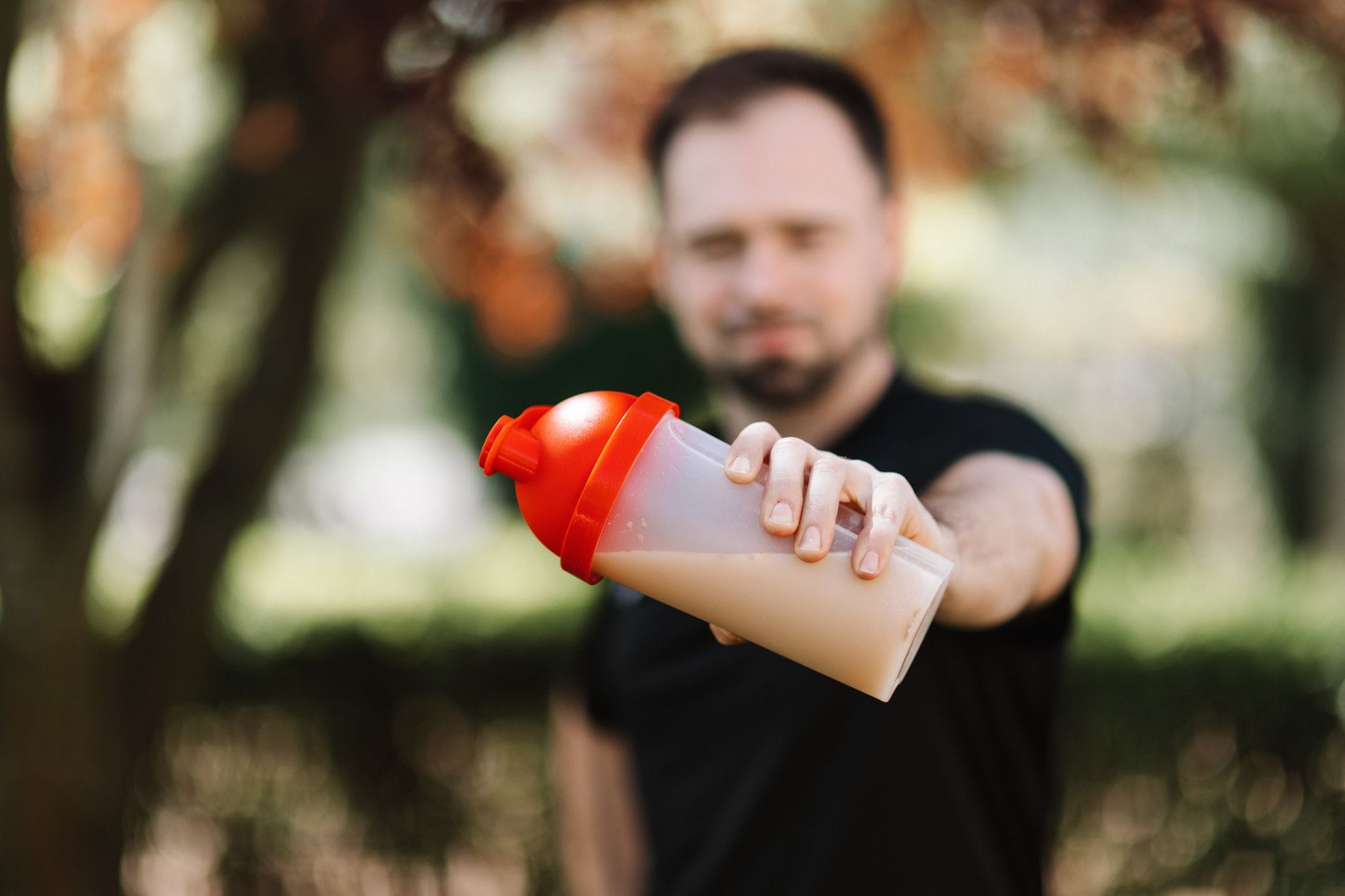Mężczyzna trzyma shaker z odżywką na tle zieleni na zewnątrz