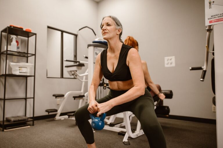 Starsza kobieta wykonuje przysiady z kettlebell na siłowni